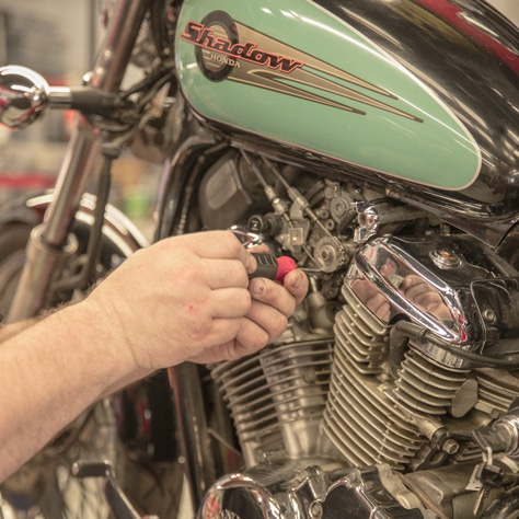 A technician's hands using a screwdriver to adjust a screw on a motorcycle