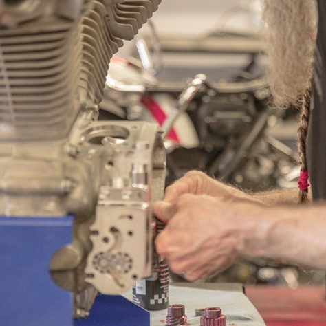 A technician's hands working on a motorcycle engine.